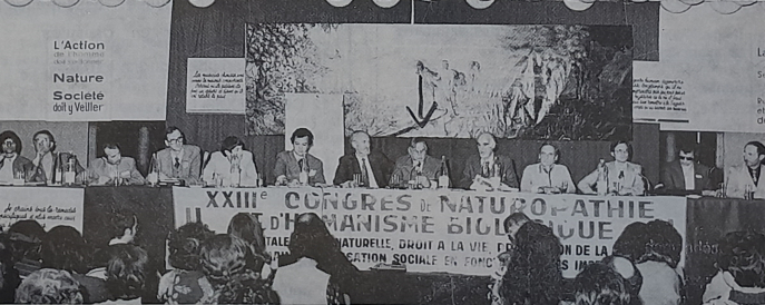 Photographie de la tribune du Congrès de naturopathie et d’humanisme biologique de 1978. La flèche indique le président d’honneur de la FFN, un certain Alexandre Bayait, à sa gauche se trouve Pierre-Valentin Marchesseau. BnF