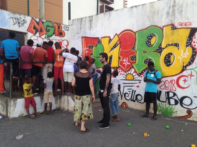 une quinzaine de jeunes hommes noirs devant un mur avec des graffitis accompagnés de 2 adultes blancs